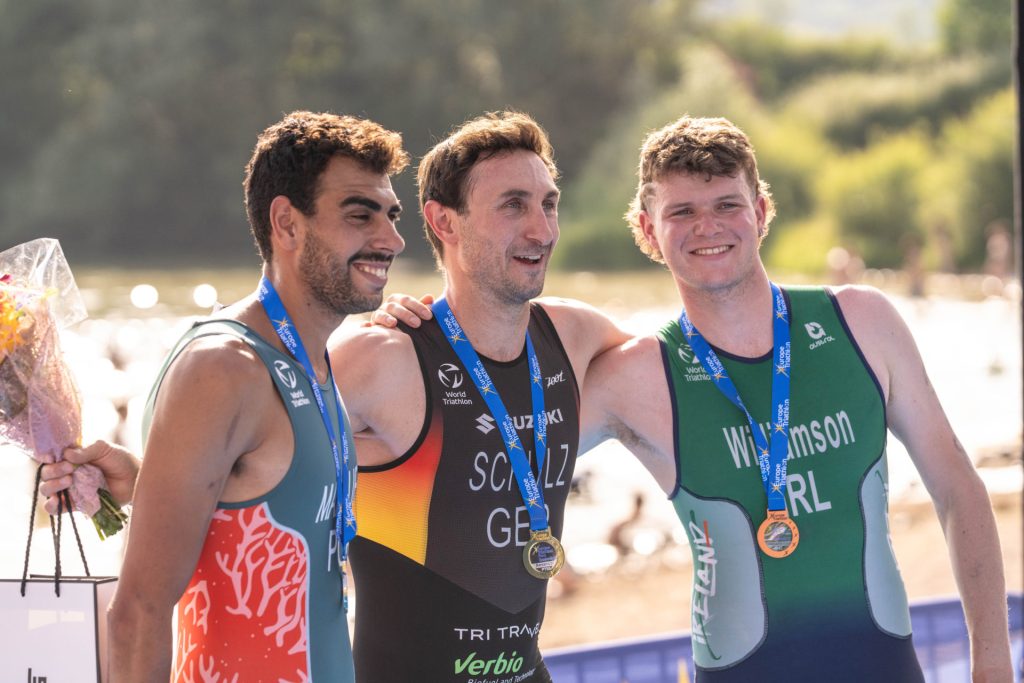 Tom Williamson (right) poses with his medal and with his arms around fellow podium winners