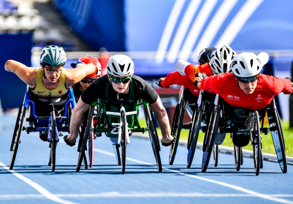 Shauna Bocquet wearing black competition kit pushes her wheelchair alongside 5 other athletes