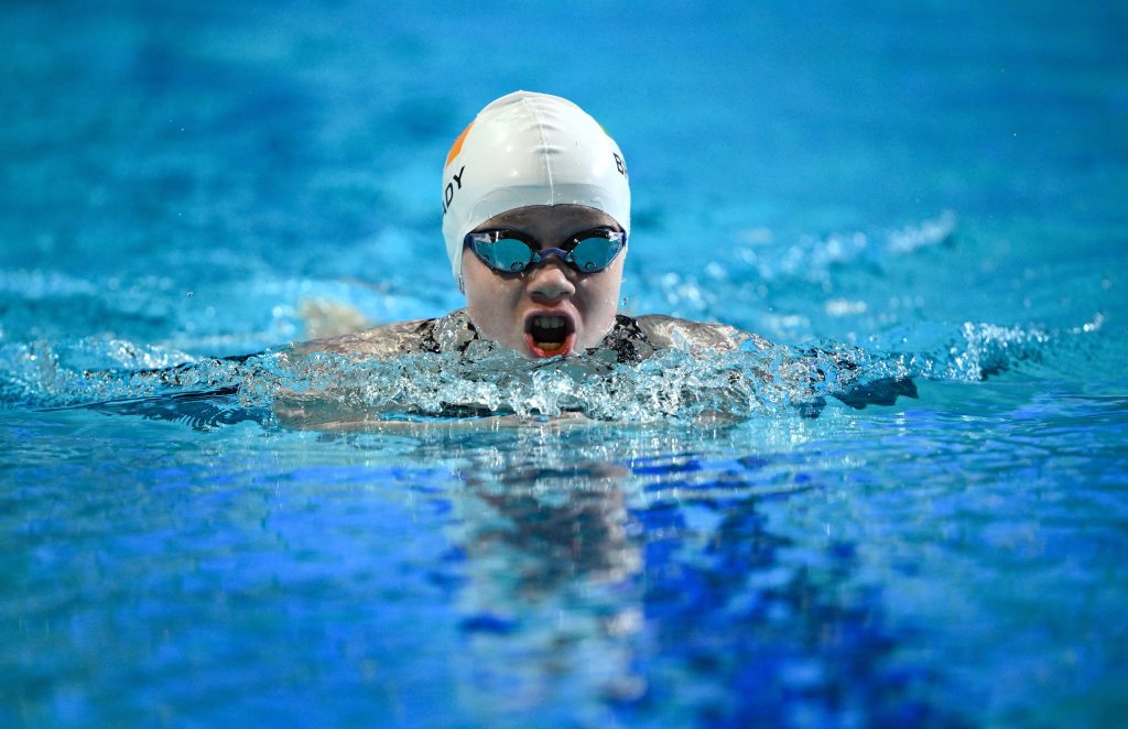 Dearbhaile Brady swims butterfly in a blue pool, wearing an Ireland swim cap and goggles, with water splashing around her face.