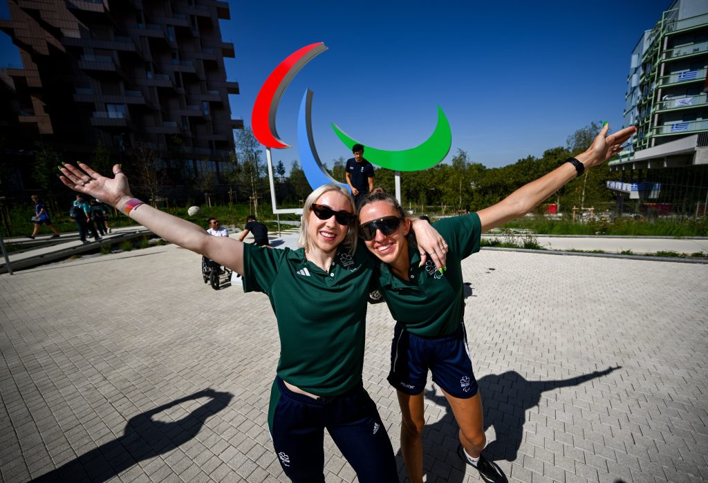 Irish athletes Orla Comerford and Greta Streimikyte wearing green leisure kit smiling with arms outstretched and the other arm around each others shoulders