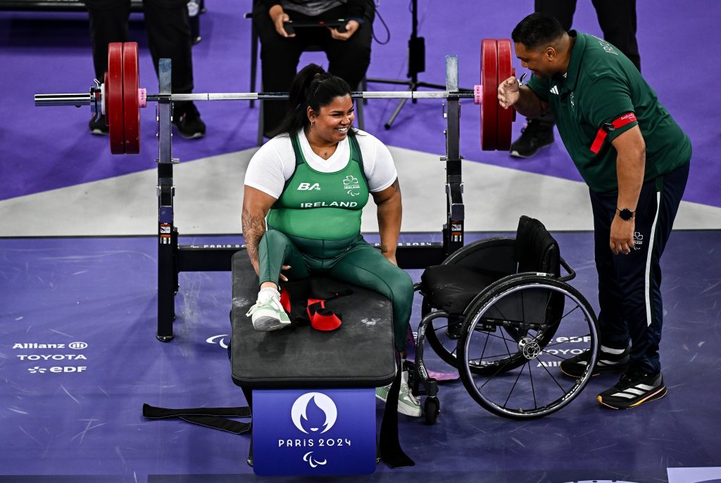 Britney Arense smiling with her coach/father after one of her lifts at the Paris Games. Sitting on weight lifting bench