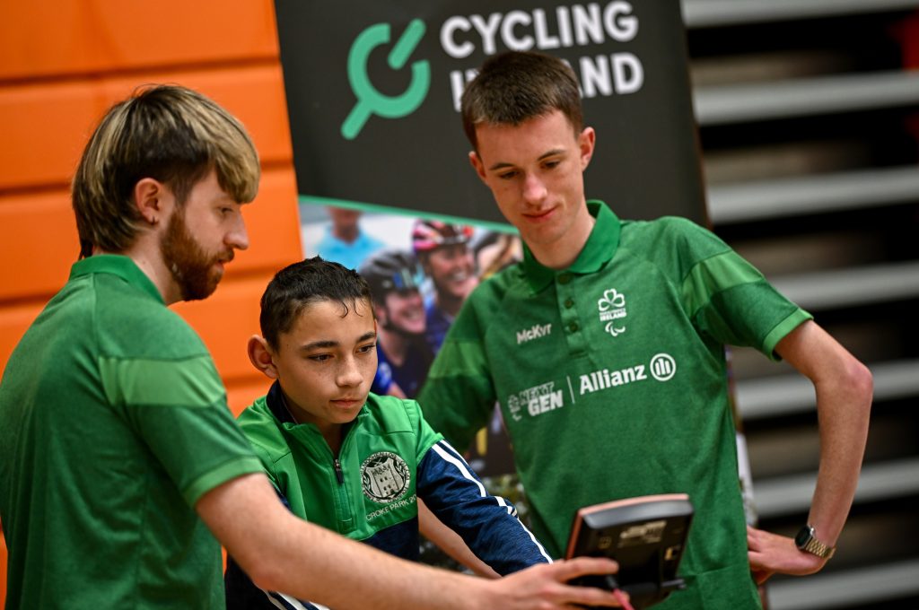 Darragh Whelan (left), Shane Murphy (centre) and Cormac O’Callaghan (right) look at a cycling screen together inside a sports hall.