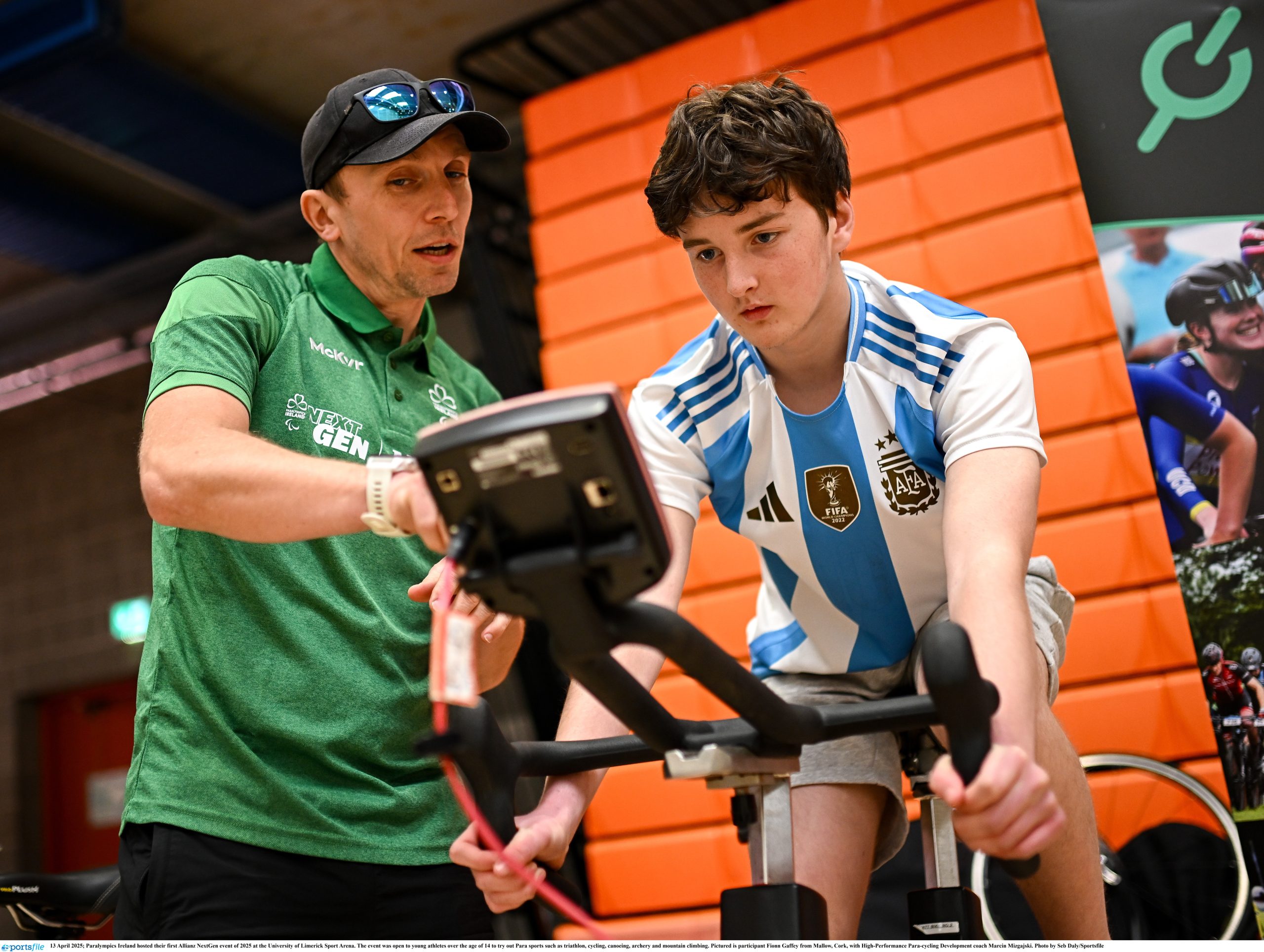 A boy on an exercise bike looks at the screen as his coach speaks to him
