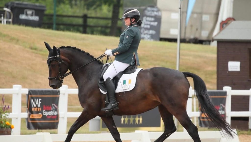 Katie Reilly Para dressage in competition on her horse wearing green irish competition jacket. Brown horse.