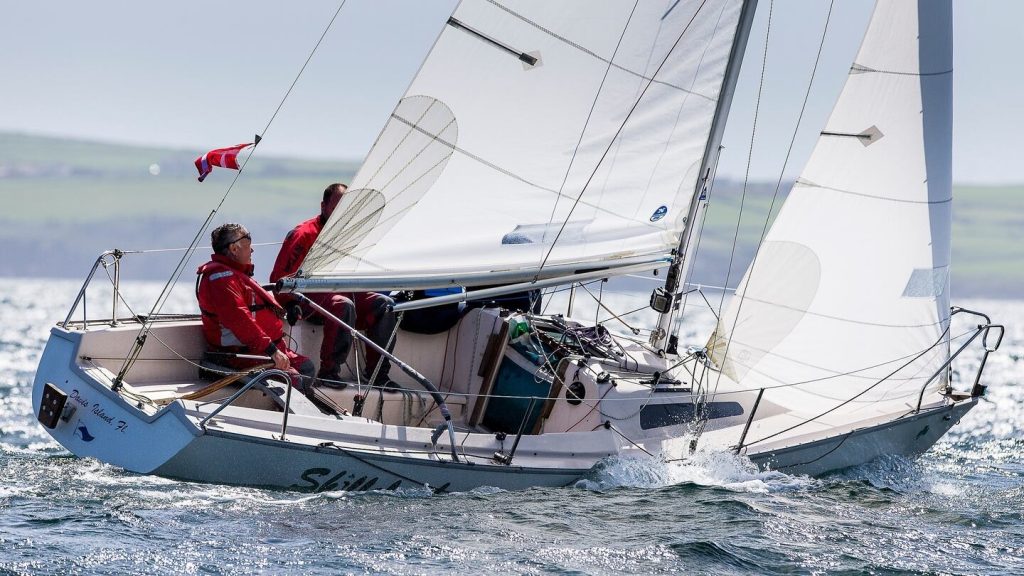 Two men wearing red sailing a white sailing boat on a sunny day.