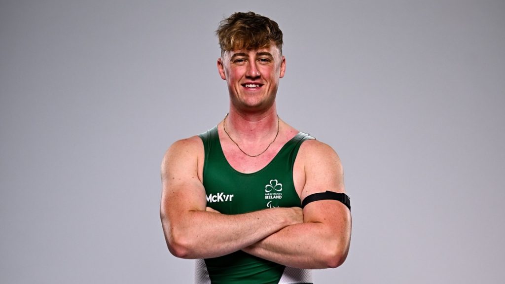 Tiarnán O’Donnell standing with arms crossed, wearing a green Paralympics Ireland rowing vest, photographed against a plain studio background during the Team Ireland Paralympic Games announcement.