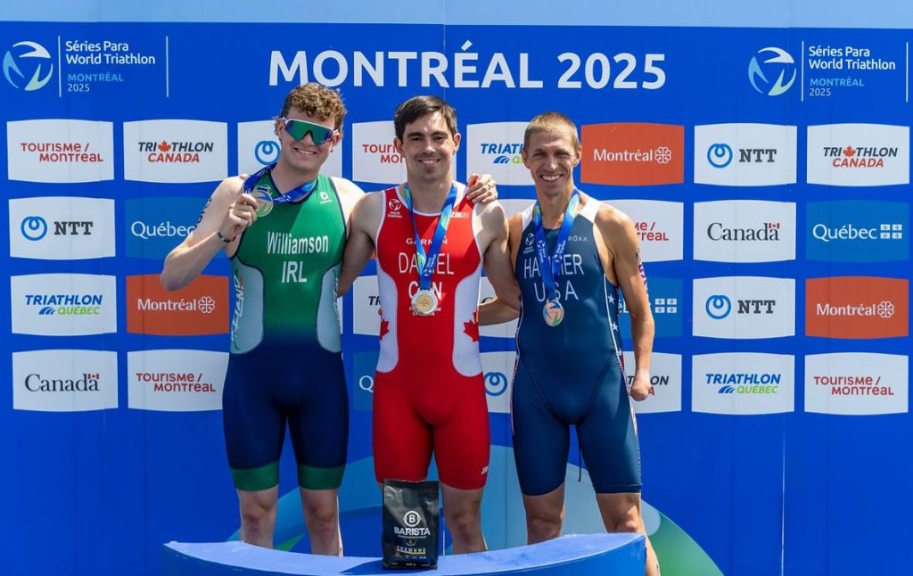 Tom Williamson, in green of Ireland, stands on the podium with his bronze medal at the World Triathlon Para Series in Montreal, alongside the gold and silver medallists.
